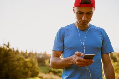 Portre portre parkta ücretsiz kablosuz kullanarak onun akıllı telefon aracılığıyla uygun genç atlet erkek manifatura mesajları. Sabah koşu sırasında müzik ve açık çalıştırmak çekici runner. 