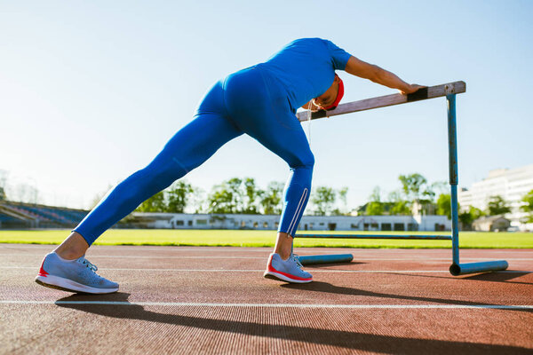 Нижний хорионный вид красивого спортсмена мужские упражнения с препятствием на беговой дорожке в солнечный день. Наружная тренировка бегуна с препятствием на стадионе. Люди и спорт
. 