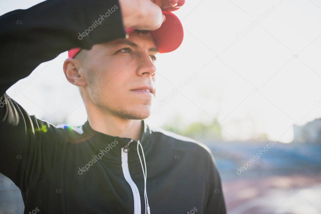Horizontal closeup shot of young athletic man looking away posing on the stadium. Attractive runner preparing for a morning jog and run outdoor. Sport, people and lifestyle concept.