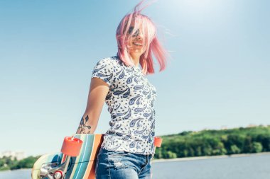 Çekici modern bir kadeh pembe saçlı longboard elinde üfleme olan güzel seksi kadın. Avrupa kadın longboard ile yürüyüş gülümseyen güneşli hava keyfini çıkarın. Sağlıklı yaşam tarzı.