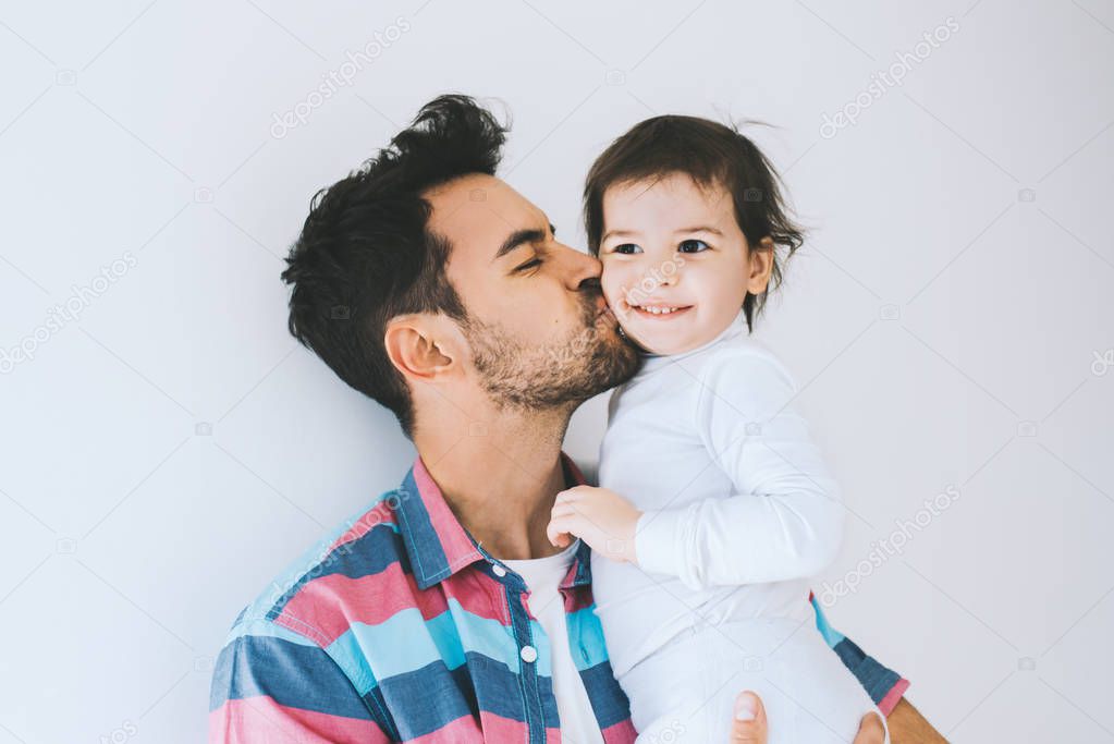 Attractive close up portrait of hipster father kissing his little daughter. Young dad is enjoying time with his child. Handsome father with little girl. Happy father and daughter. Lifestyle family.