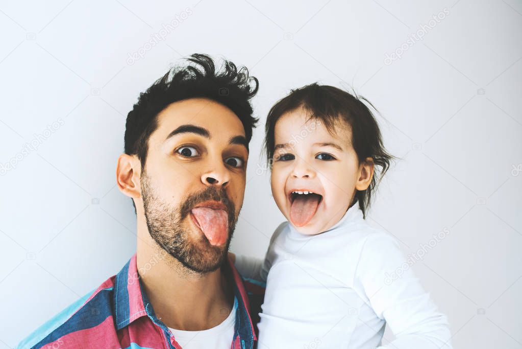 Happy father and beautiful little daughter sticking tongue out, isolated over a white background. Funny faces. Fatherhood. Dad play activities with his girl together shows tongues. Lifestyle family.