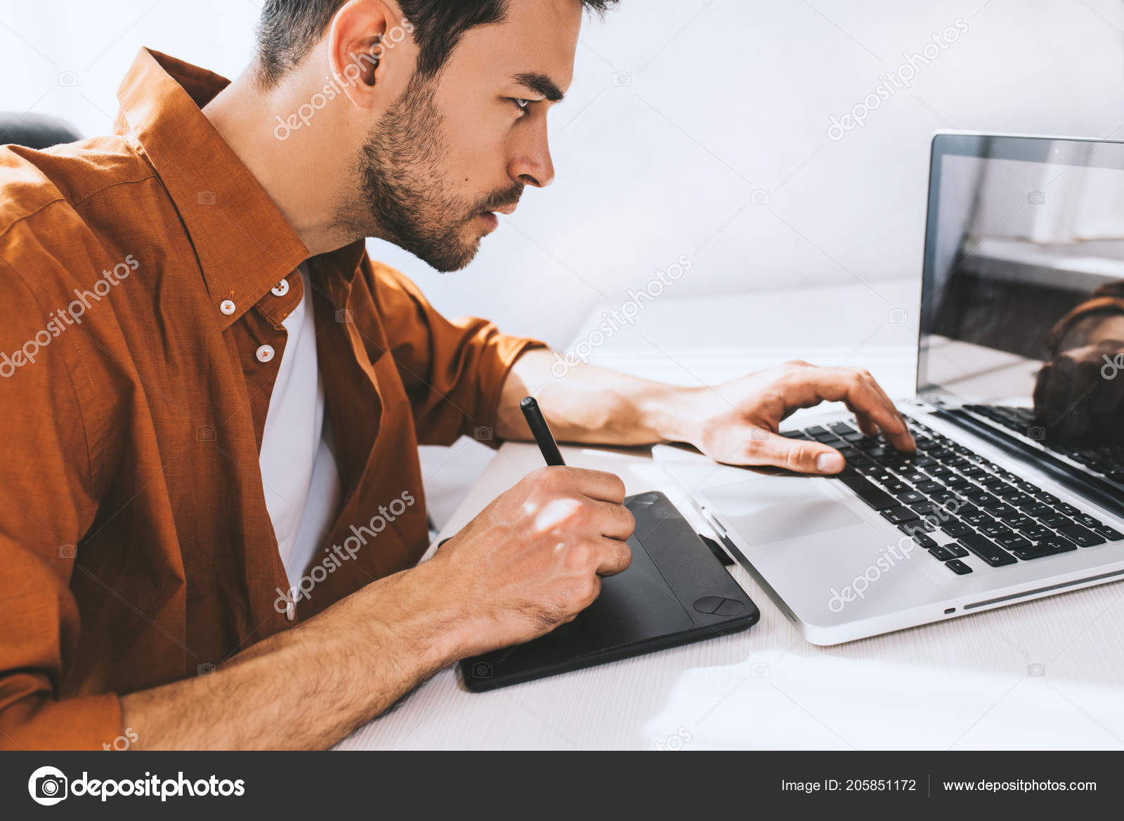 深刻な思慮深い表情でノート パソコンの前に座っている男性のフリーランサーを集中しました 若いデザイナーや建築家事務所で座って仕事のペンとノート パソコンを使用してのシャツ ストック写真 C Iuricazac