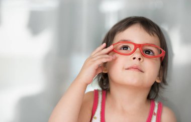 Ararken akıllı mutlu beyaz sevimli küçük öğrenci kız portresi. Meraklı mutlu güzel bebek kız kırmızı gözlük takıyorum. Eğitim kavramı.
