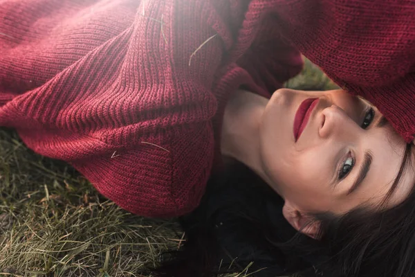Yan görünümü weahter zevk çim üzerinde yalan gülümseyen, örme kazak giyen ve kameraya, arıyorum bir güzel genç seksi esmer kadın portresi. Gevşeme, seyahat ve insanlar kavramı.