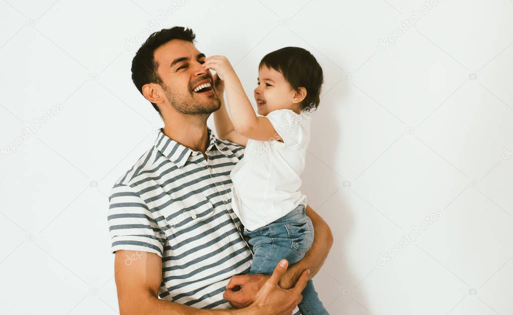 Happy cute little girl and her handsome father are hugging and playing together against white background. Playful smiling daughter touch daddy's nose with finger having fun with dad.Happy relationship