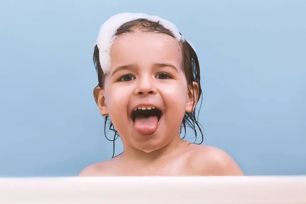 有趣的快乐的幼儿宝宝洗澡泡沫泡沫 小孩在浴缸里露出舌头 微笑的孩子在浴室的蓝色背景 幼儿洗涤和沐浴 — 图库照片