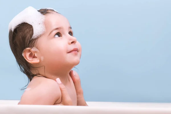 風呂に入って泡泡と遊ぶかわいい幼児赤ちゃんの肖像画 見上げるバスタブで 幼い子供 青の背景に浴室で子供を取る 乳児の入浴 ヘルスケア — ストック写真
