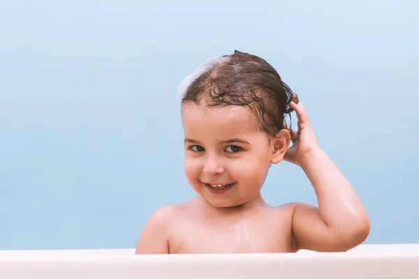 楽しいかわいい幸せな幼児赤ちゃん入浴泡泡で遊んで 髪を洗います バスタブで 幼い子供 青の背景に浴室で子供を笑っています 乳児の入浴 ヘルスケア — ストック写真