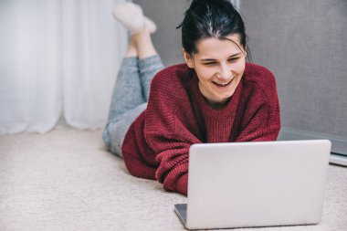 Mutlu genç kadın istimal radyo arkadaşıyla konuşuyor. Casual erkek gülümseyen ve halı üzerinde dizüstü kullanarak online alışveriş web sitesi tarama yaparken yalan. İnsanlar ve yaşam tarzı kavramı