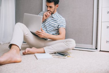 Akıllı neşeli genç Avrupa adam şık gömlek kucak, düşünme ve iş başlangıç için uyarı üzerine açık dizüstü bilgisayarla evde katta oturan samimi bir kadeh. İnsanlar ve yaşam tarzı kavramı.