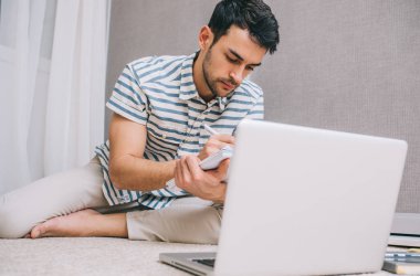 İnsanlar, iş ve yaşam tarzı kavramı. Oda açık dizüstü bilgisayar önünde yerde oturan genç beyaz adam öğrenci odaklı. Ciddi Avrupa erkek öğrenci ders öğrenme.