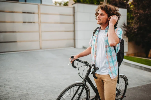 Side view of young handsome hipster male with curly hair with backpack, stopped the bike on the city street for ecological life. Man student bicycling with bycicle to the college. People, lifestyle