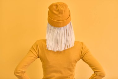 Arka görünümü stüdyo portre ile bel, ellerinde sarı elbiseler giymiş çekici sarı saçlı kadının sarı duvarda reklam veya bilgi metinlerinin kopya alanı boş duvara bakarak   