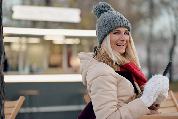 Mutlu güzel kadın kafeterya Teras şehir sokakta, otururken metin mesajları gönderme. Konuşma sırasında tatil için akıllı telefon kullanarak güzel kadın gülümseme. Telefonda sohbet öğrenci  