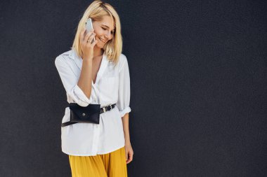 gülümseyen ve gri binalar duvara karşı cep telefonu konuşurken ayakta sarışın kadın