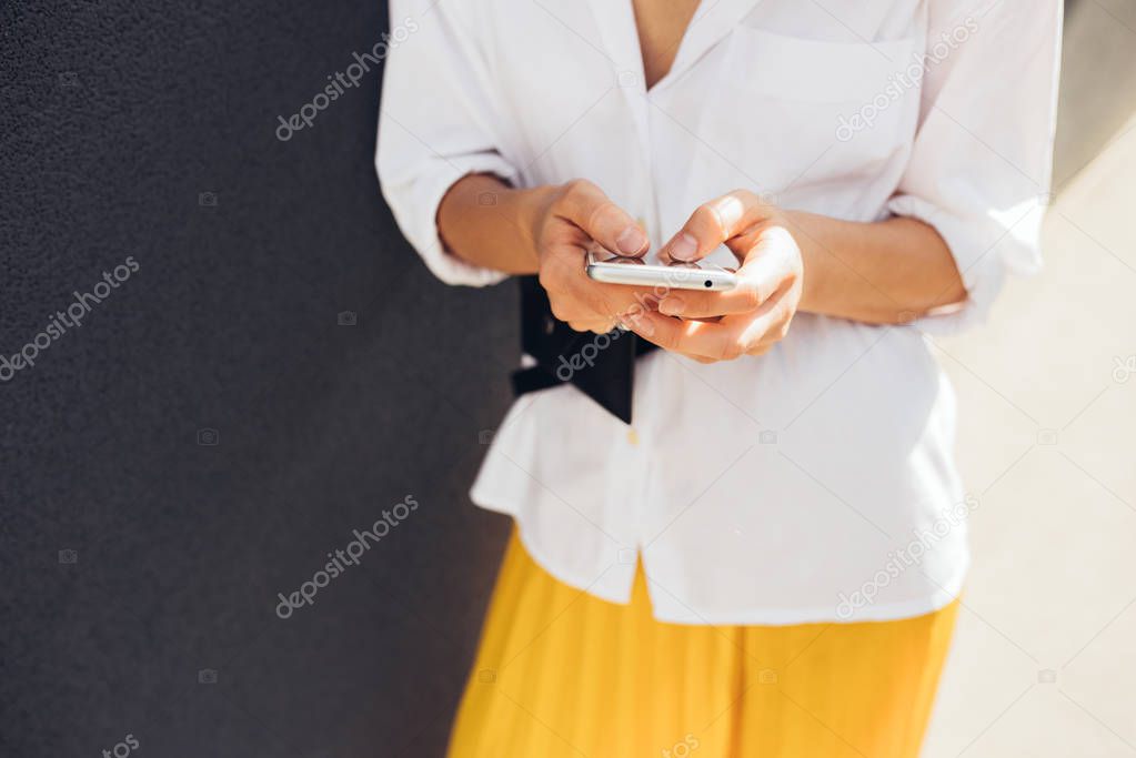 Caucasian female texting message on mobile phone on gray wall outdoor 
