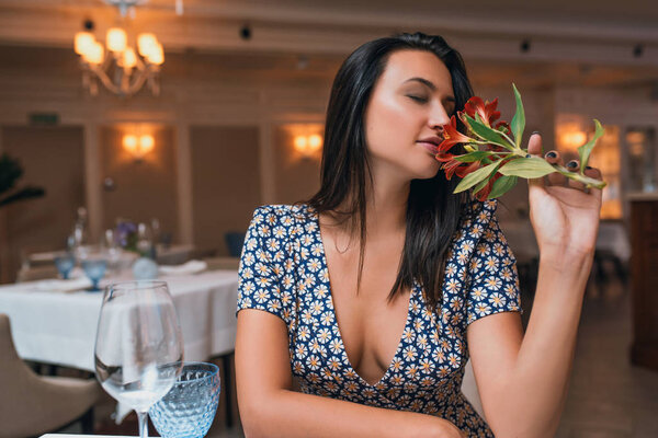 brunette young woman sitting in restaurant and smelling flowers