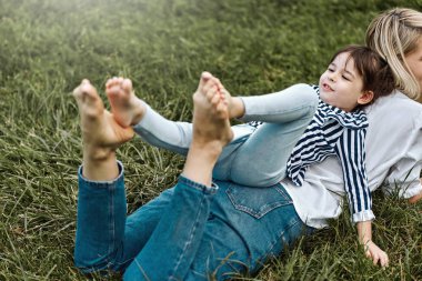 Yatay görüntü yalan ve sevimli küçük kızı ile açık havada yeşil çimenlerin üzerinde oynarken güzel kadın. Mutlu çocuk ve anne parkta birlikte vakit. Anneler günü kavramı