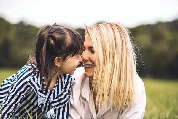 Young beautiful woman cuddling with her little daughter in the park. Loving mother and daughter lying on the gree grass in the park. Mom and kid have fun outside. Happy family. Good relationship.