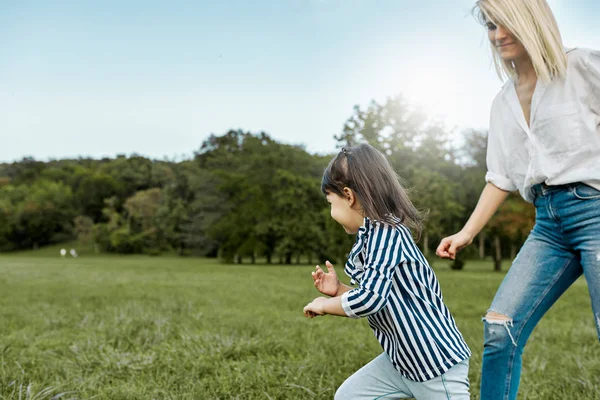 Happy pretty little girl playing catch me with her mother on green grass in the park. Loving beautiful woman and her daughter spending time together. Mom and kid has fun. Mother\'s day
