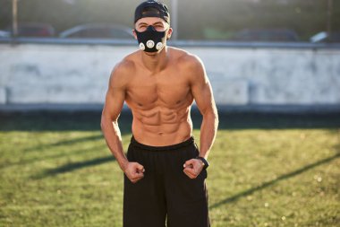 Nefes egzersizleri daha önce açık havada poz kasları üzerinde artırmakta Kafkas fitness kas maskeli adam portresi. Uzay kopyalayın. Yakışıklı gömleksiz sporcu stadyum üzerinde egzersiz yapıyor.