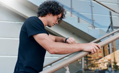 Genç işadamı yan görünüm geç bir röportaj ve kol saati, üst katta şehir sokak yürüyüş, seyir için vardır. Karşı bina açık merdivenlerde poz kıvırcık saçlı erkek. İnsanlar kavramı