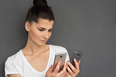 Beyaz T-shirt görünüyor üzerinde iki monitörün cep telefonu için güvensiz esmer beyaz genç kadının yatay atış seçin gri arka plan, kopya alanı, metniniz için satış için iyi bir reklam.