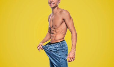 Stüdyo imge-in genç beyaz diyet sonra büyük mavi kot pantolon giyen adam seksi gövde gösterilen uygun yatay yan görünüm. Mutlu gülümseyen adam kilo kaybettikten sonra. Uzay kopyalayın. Diyet, sağlıklı yaşam konsepti.