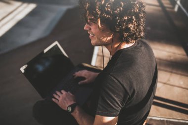 Dikiz erkek arkadaşları ve müzik için ücretsiz kablosuz bağlı kulaklık ile online sohbet için dizüstü bilgisayar kullanarak kıvırcık saçlı bir kadeh. Yakışıklı adam manifatura iletileri.