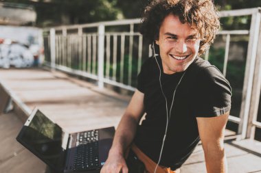 Hapy dizüstü online müzik dinlemek için kulaklık kullanarak arkadaşlarınızla sohbet kullanarak kıvırcık saçlı erkek portresi için ücretsiz kablosuz bağlı. Erkek blogger sonrası bilgisayarda Web sitesinde yayımlama.