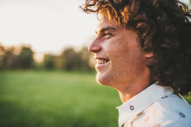 kıvırcık saçlı parkta güneşli gülümseyen mutlu beyaz genç adam yan görünüm