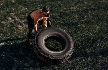 Yukarıdan yakışıklı fitness kas erkek maskeli nefes egzersizleri üzerinde büyük lastik açık havada yapıyor kaslar üzerinde artırmakta görüntüleyin. Metin için yer kopyalayın. Gömleksiz sporcu stadyum üzerinde egzersiz yapıyor.