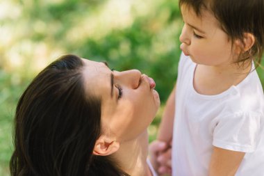 Birbirlerine öpücük üfleme neşeli güzel anne ve sevimli kızının oynarken dışarıda kırpılmış yakın çekim. Anne ve onun güzel çocuk parkta oynamak. İyi ilişki içinde aile portresi