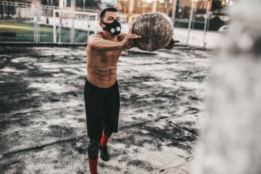 Genç vücut geliştirmeci erkek sağlık topu beton zemin için reklam kopya alanı ile açık üzerine eğitim maskesinde ile yapıyor. Egzersiz yaparken beyaz gömleksiz sporcu