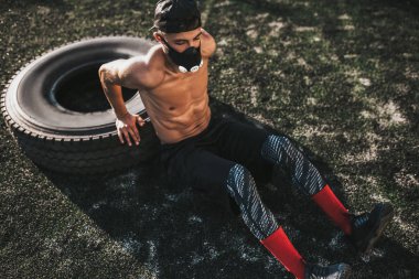 Açık havada lastik üzerinde triceps için egzersiz yapmak kaslara nefes üzerinde artırmakta maskede oturan beyaz fitness kas erkek. Uzay kopyalayın. Gömleksiz sporcu crossfit egzersiz yapıyor