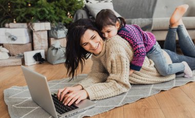 Güzel mutlu genç kadının alışveriş online laptop rahat Noel iç kapalı atış. Yerde yatarken anne sonraki Noel ağacı ve kanepe ve kızı ona hediye alışveriş kucaklamak.