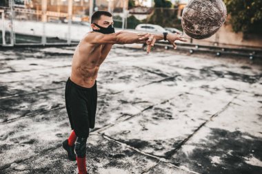 Maske beton zemin için reklam kopya alanı ile açık üzerine tıp top ile görüntü atletik erkek yapmanın uygular. Egzersiz yaparken beyaz gömleksiz sporcu 