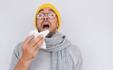 Gri kazak, sarı şapka ve gözlük, üfleme burun ve doku içine hapşırma hasta yakışıklı adam portresi. Grip, virüs ya da anti solunum erkek var. Sağlıklı, tıp ve insanlar kavramı