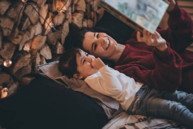 Oldukça mutlu anne ve küçük kızı okuma kitabı yatakta rahat ile yan görünüm ve Noel dekorasyonu. Güzel kadın ve sevimli küçük kız edebiyat var. Aile ve insanlar kavramı