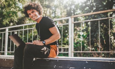 Yatay görüntü dizüstü bilgisayar kullanan ve kaldırımda otururken gülümseyen neşeli beyaz erkek. Genç iş adamı dışında serbest. 