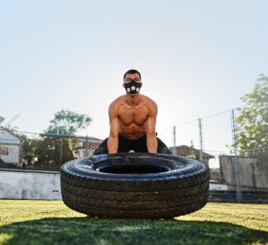 Açık havada stadyumda büyük lastik ile egzersiz yaparak kasları nefes üzerinde artırmakta maskede poz beyaz kas genç erkek. Metin için yer kopyalayın. Gömleksiz sporcu egzersiz, sağlıklı yapıyor
