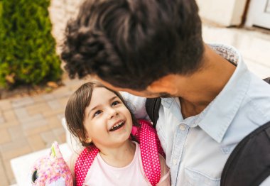 Closeup üstten görünüm portre yakışıklı genç baba kızı gözbebeği sonra okul öncesi kucaklamak. Babası onu mutlu duygu gülümseyen isteyen sevimli küçük kız. Her ikisi de ev önünde oturuyorlar