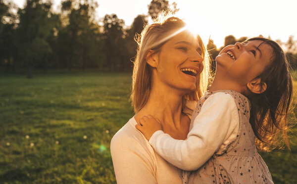 Порт веселой счастливой девочки, играющей с матерью на свежем воздухе на закате. Портрет женщины и ее милого ребенка, смеющегося в парке снаружи. Счастливые эмоции. С Днем Матери. Материнство, детство
