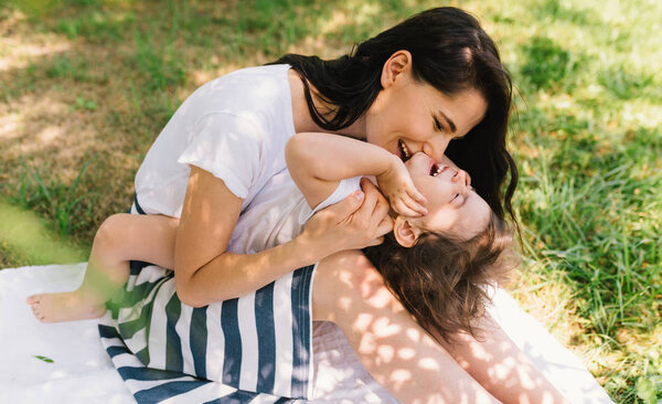 Horizontal shot of beautiful happy mother and her little smiling daughter play outdoor. Cute European mom and her child playing in the park together. Happy family. Happy Mother's Day. Motherhood.