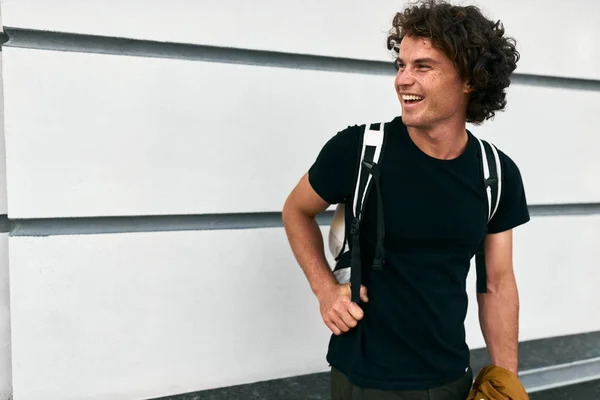 laughing handsome student man with curly hair posing and standing against white wall