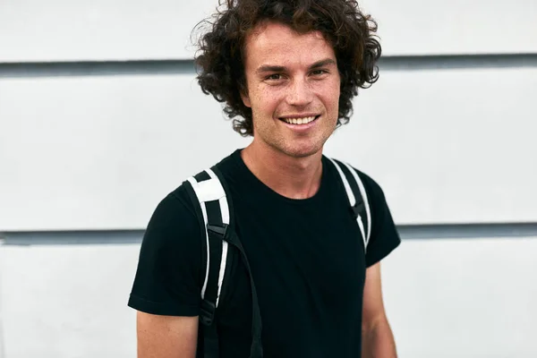 smiling handsome student man with curly hair posing and standing against white wall