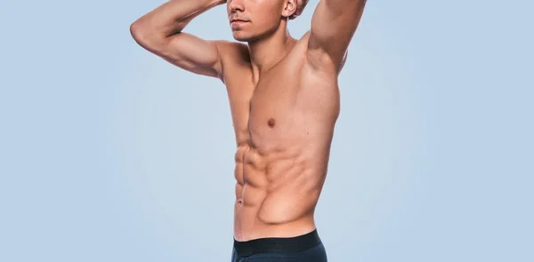 Horizontal image of fitness muscular male model in black underwear showing his abdominal press on a blue background. Cropped head portrait of sporty healthy strong athletic man with sexy torso.