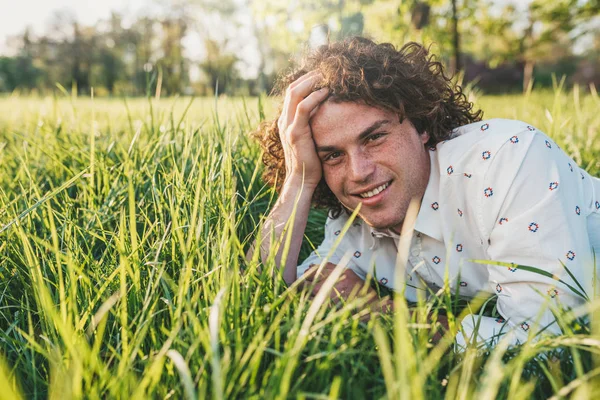 Jovem Caucasiano Feliz Com Cabelo Encaracolado Sorrindo Deitado Grama Verde — Fotografia de Stock