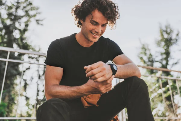 Happy smiling young male wears black t-shirt and wears wirstwatch on the street. Cheerful man posing for advertisement with copy space, outdoor in the city street. People concept